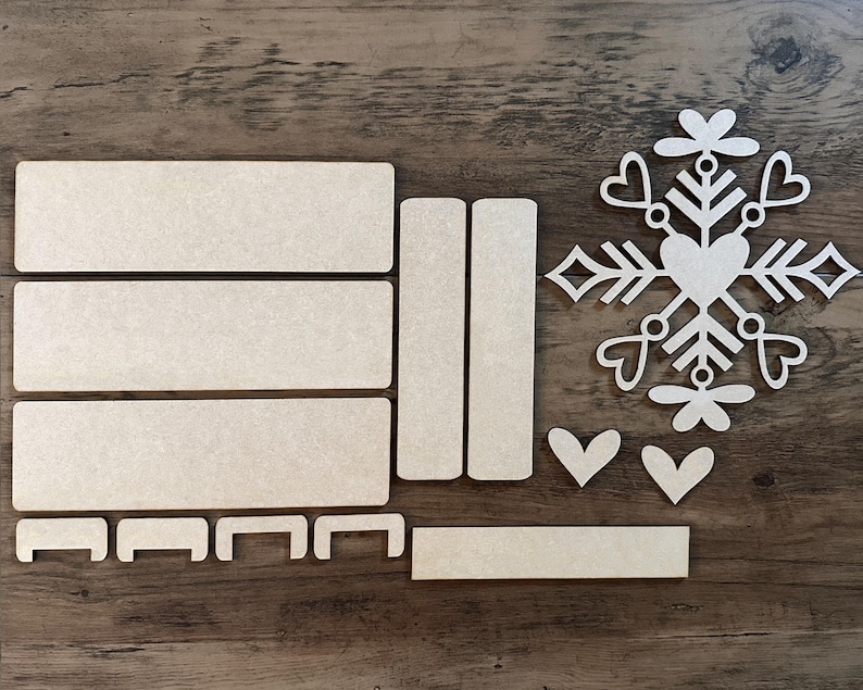 Puede incluir: Un conjunto de piezas de artesan&iacute;a de madera para crear un adorno de copo de nieve. El conjunto incluye una forma de copo de nieve, un coraz&oacute;n y varias piezas rectangulares.