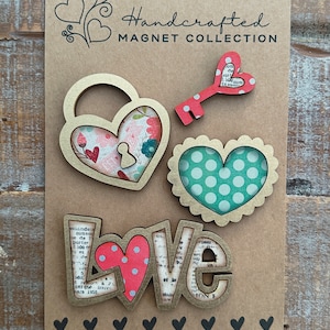 May include: Set of five wooden magnets with a love theme. The magnets feature a heart-shaped lock and key, a heart with polka dots, and the word "LOVE" with a heart in the letter "O". The magnets are decorated with a vintage paper design and have a gold-colored trim.