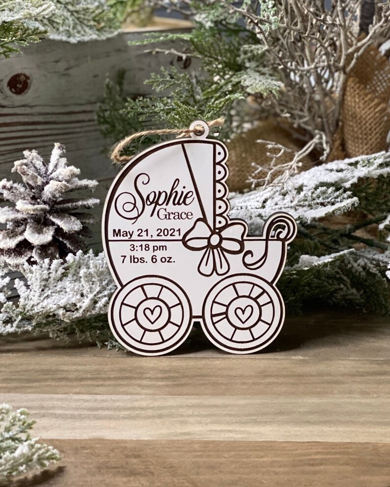 May include: White wooden baby carriage ornament with a brown inscription that reads "Sophie Grace, May 21, 2021, 3:18 pm, 7 lbs. 6 oz."
