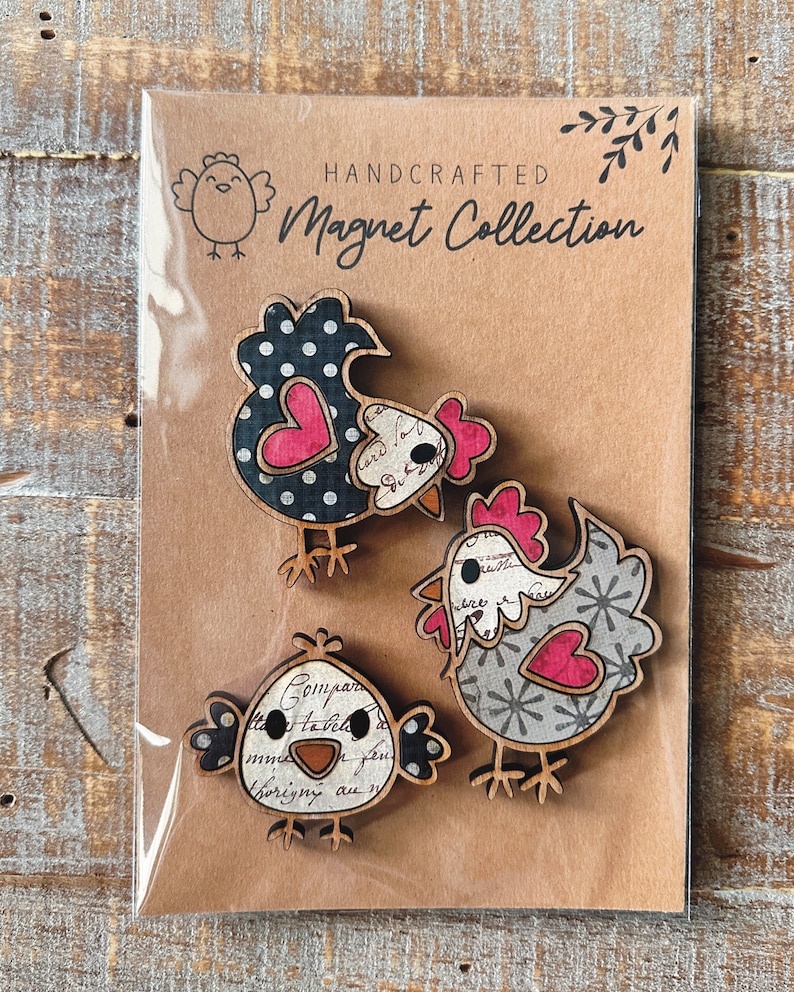 Puede incluir: Conjunto de tres imanes de pollo de madera hechos a mano. Los pollos est&aacute;n decorados con lunares negros y blancos, copos de nieve grises y blancos y un patr&oacute;n floral vintage. Cada pollo tiene un coraz&oacute;n rosa en el pecho. Los imanes est&aacute;n empaquetados en una tarjeta marr&oacute;n con el texto "HANDCRAFTED Magnet Collection".
