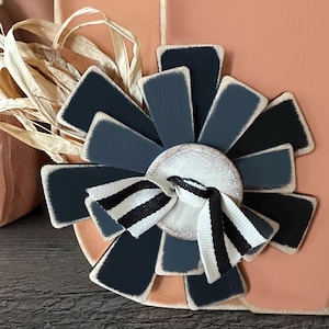 Pode incluir: Uma flor de madeira preta e branca com um la&ccedil;o branco e preto listrado no centro. A flor &eacute; feita de v&aacute;rias pe&ccedil;as de madeira pintadas de preto e branco.