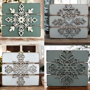 Puede incluir: Cuatro letreros de madera con diferentes dise&ntilde;os de copos de nieve. Cada letrero est&aacute; hecho de tres tablones de madera pintados en tonos de verde y blanco. Los copos de nieve est&aacute;n cortados de madera blanca y se superponen a los tablones.