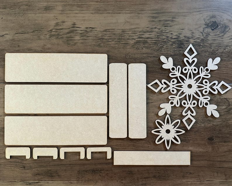 Puede incluir: Un conjunto de piezas artesanales de madera para crear un adorno de copo de nieve. El conjunto incluye un dise&ntilde;o de copo de nieve, una estrella y varias piezas rectangulares.