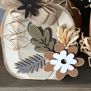Pode incluir: Uma ab&oacute;bora de madeira branca decorada com um la&ccedil;o de juta marrom, flores pretas, folhas marrons e verdes e flores marrons e brancas. A ab&oacute;bora &eacute; decorada com barbante marrom e branco.