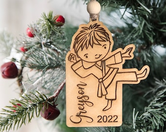 May include: A wooden Christmas ornament featuring a cartoon illustration of a child in a karate pose. The ornament is personalized with the name "Greyson" and the year "2022".