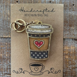 May include: Handcrafted wooden keychain or bag tag shaped like a coffee cup with a red heart and polka dots. The tag is attached to a gold metal key ring.