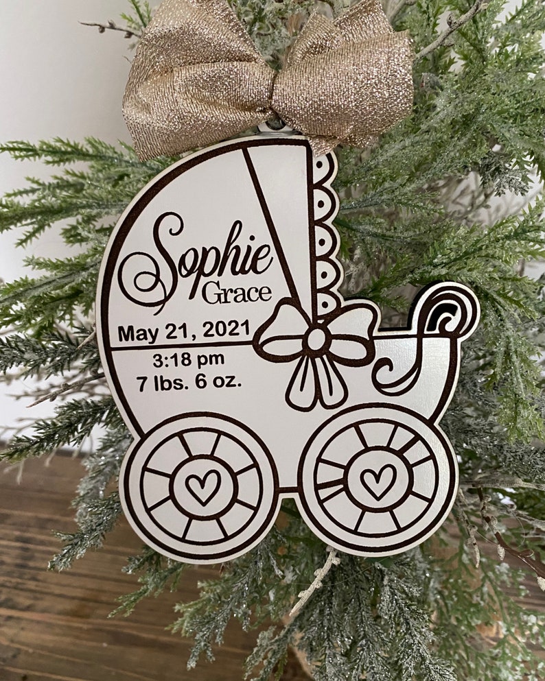 May include: White wooden baby carriage ornament with the name "Sophie Grace" and the date "May 21, 2021" and the time "3:18 pm" and the weight "7 lbs. 6 oz."