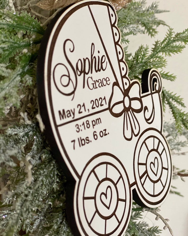 May include: White wooden baby carriage ornament with a black outline. The ornament is personalized with the name "Sophie Grace", the date "May 21, 2021", the time "3:18 pm", and the weight "7 lbs. 6 oz."