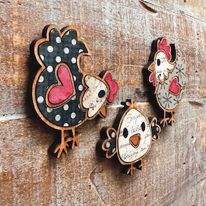 Puede incluir: Tres adornos de pollo de madera con patrones de lunares negros y blancos, corazones rojos y texto de estilo vintage. Los pollos est&aacute;n en varias poses, incluyendo de pie, sentados y mirando hacia un lado.