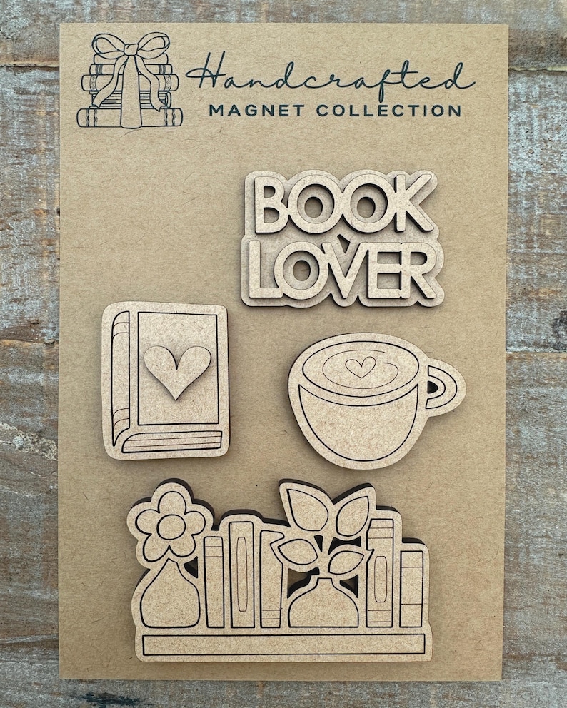 May include: A collection of handcrafted wooden magnets on a tan background. The magnets include a stack of books with a bow, the words "BOOK LOVER", a book with a heart, a coffee cup with a heart, and a shelf with books, plants, and a flower.