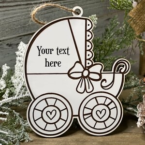 May include: White wooden baby carriage ornament with a bow and hearts on the wheels. The ornament has the text "Your text here" on it.