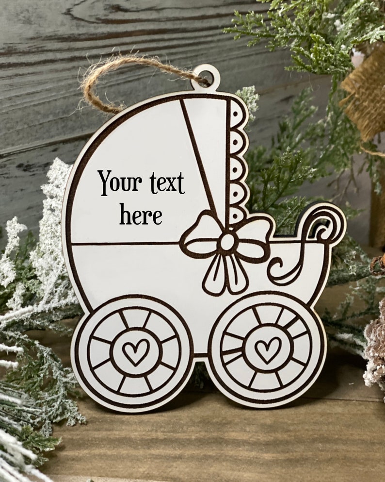 May include: White wooden baby carriage ornament with a bow and hearts on the wheels. The ornament has the text "Your text here" on it.