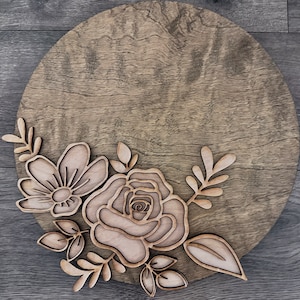May include: A round wooden sign with a floral design. The design features a large rose and smaller flowers with leaves.