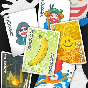May include: A collection of colorful Joker playing cards with various illustrations, including a banana, a smiley face, and a campfire scene. The cards are arranged with a clown face and white hands in the background.
