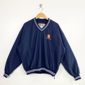 May include: A navy blue long-sleeve pullover windbreaker jacket featuring a V-neck collar with white stripes, ribbed cuffs, and an orange embroidered Syracuse logo on the chest. The jacket includes a side zipper and a Russell Athletic brand label.