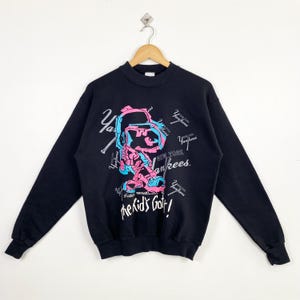 Può includere: Felpa girocollo nera con un personaggio dei cartoni animati rosa e blu, con la scritta "New York Yankees" e "the kid's got it!" in bianco. La felpa ha maniche lunghe e scollo tondo.