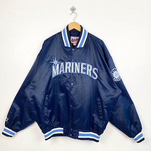 May include: A navy blue satin jacket featuring the word "MARINERS" in white across the chest. The jacket has a white and light blue striped collar, cuffs, and hem. A team logo is on the sleeve.