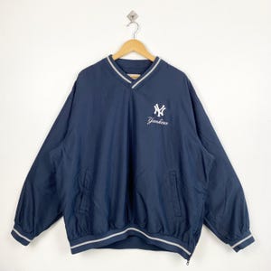 Op de afbeelding: Marineblau Yankees pulloverjack met een V-hals, witte en grijze afwerking en een voorzak. Het Yankees-logo en de tekst zijn wit op de borst geborduurd. De jas heeft lange mouwen en een trekkoord in de zoom.