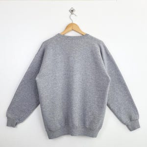 Op de afbeelding: Een grijs gem&ecirc;leerde sweatshirt hangt aan een houten hanger tegen een witte achtergrond. De crewneck sweatshirt heeft lange mouwen en geribde manchetten en zoom. Het kledingstuk is gemaakt van een zacht, comfortabel materiaal.