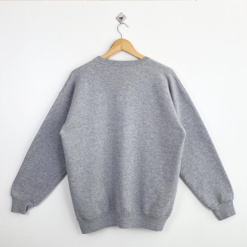 Op de afbeelding: Een grijs gem&ecirc;leerde sweatshirt hangt aan een houten hanger tegen een witte achtergrond. De crewneck sweatshirt heeft lange mouwen en geribde manchetten en zoom. Het kledingstuk is gemaakt van een zacht, comfortabel materiaal.