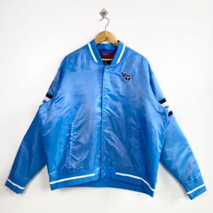 May include: Light blue satin bomber jacket with white and black striped accents on the sleeves. Features a white collar and cuffs with a blue and white striped design. The jacket has a snap-button closure and a team logo patch on the chest.
