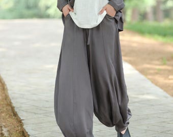 May include: A woman wearing a gray cardigan, a white top, and gray harem pants. The outfit is loose-fitting and comfortable. The pants have a drawstring waist and gathered ankles. The woman is wearing black shoes and is walking on a paved path.