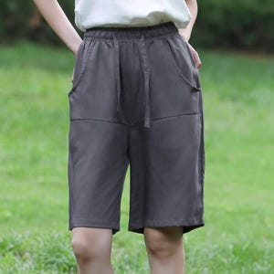 Könnte beinhalten: Dunkelgraue Shorts mit Kordelzug und Taschen. Die Shorts reichen bis zum Knie und werden mit einem weißen Neckholder-Top kombiniert. Das Outfit ist lässig und für warmes Wetter geeignet.