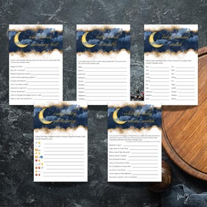 May include: Five baby shower game cards with a navy blue and gold celestial design. Each card features a crescent moon and text, including "Who Knows Mommy Best" and "Baby Word Scramble". The cards are on a wooden surface.