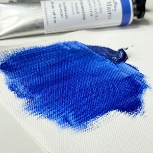 May include: A close-up of a swatch of vibrant blue oil paint on a white canvas. A partially visible tube of paint is in the background, with text that reads "Ultramarine Lapis Lazuli". The paint is thick and textured.