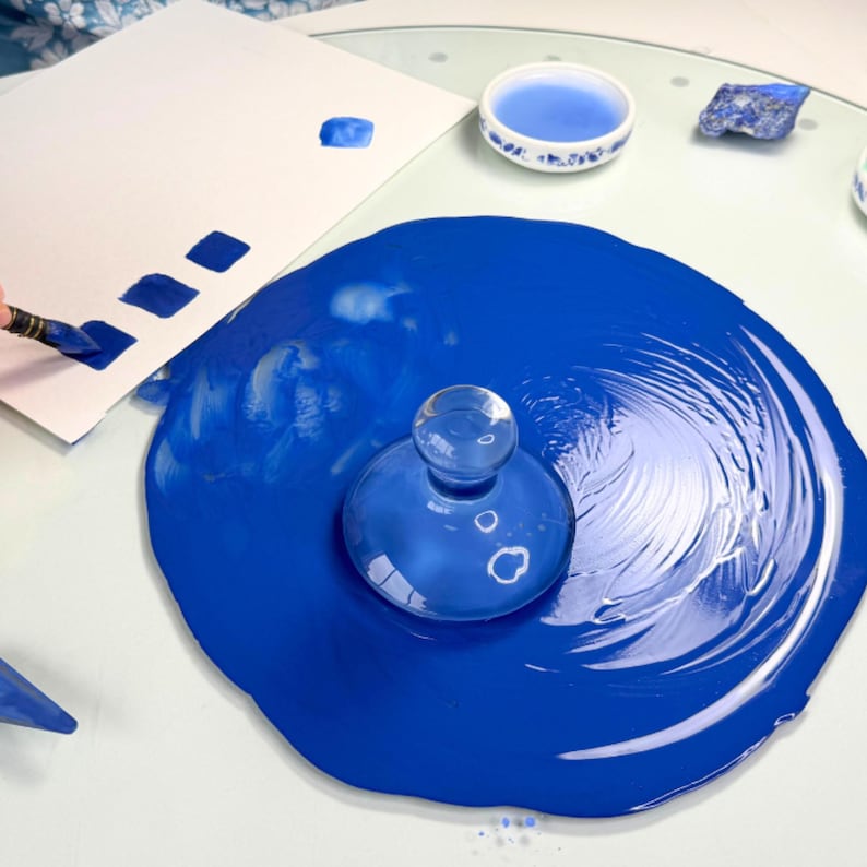 Top view of lapis lazuli ultramarine blue gouache paint milling withglass muller and artist workspace making swatches.