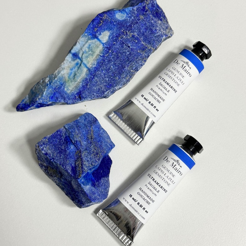 Two tubes of genuine lapis lazuli ultramarine blue gouache displayed with natural lapis lazuli stones.