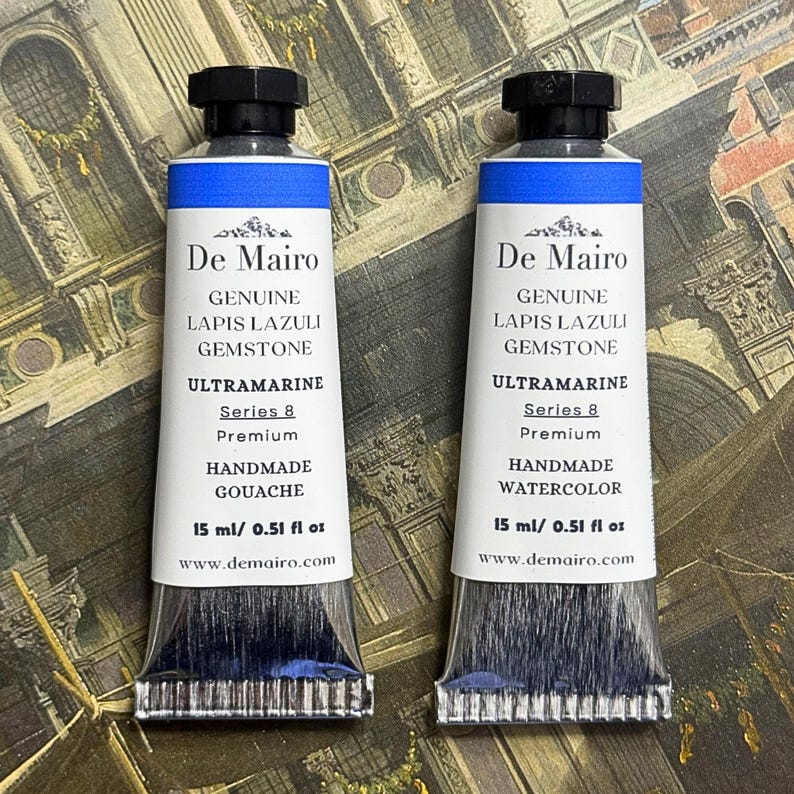 Pair of genuine lapis lazuli ultramarine blue gouache tubes displayed on vintage map style background.