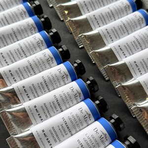 Close-up of multiple De Mairo gouache paint tubes arranged together in artist paint tray.