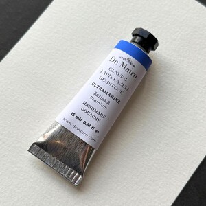 Single tube of De Mairo genuine lapis lazuli ultramarine blue gouache on textured white surface.