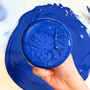 Holding the glass muller to show the creamy lapis lazuli ultramarine blue gouache paint with opaque texture after milling it.