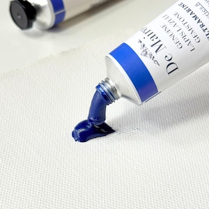 May include: A tube of De Mair&oacute; Lapis Lazuli gemstone paint, with a dark blue pigment squeezed out onto a white surface. The tube is silver with a blue cap and a blue band. The text "De Mair&oacute;" is visible on the tube.