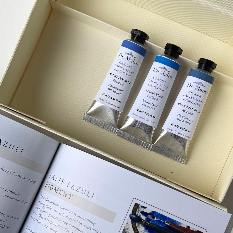 Three handmade lapis lazuli oil paint tubes with De Mairo booklet and blue pigment artwork.
