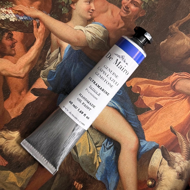 May include: A tube of De Mairo Ultramarine oil paint, labeled "Genuine Lapis Lazuli Gemstone." The tube is silver with a blue and white label, containing 40 ml / 1.69 fl oz of paint. The background features a classical painting.