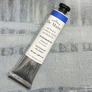 May include: A tube of De Mairo Ultramarine oil paint. The tube is white with blue accents and black cap. The text on the tube reads "Genuine Lapis Lazuli Gemstone" and "Handmade Oil Paint". The tube contains 40 ml / 1.69 fl oz of paint.