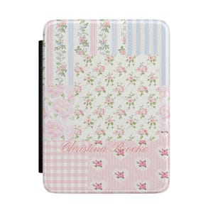 Puede incluir: Una funda rectangular con un diseño de patchwork con estampados florales, rayas y cuadros de vichy. La paleta de colores incluye rosa, blanco y azul. El texto "Christina Brooke" es visible en la funda. Una columna vertebral negra está en el lado izquierdo.