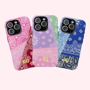 May include: Three phone cases with a paisley design in pink, purple, and blue. Each case has a different color scheme and a gold monogram. The cases are designed to fit a smartphone.