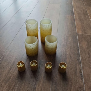 以下が含まれることがあります： さまざまなサイズの、炎のないLEDキャンドルのコレクション。 大きなキャンドルは円筒形で、黄色と金の斑点模様です。 小さな金色のティーライトキャンドルもあり、暖かく居心地の良い雰囲気を作り出しています。