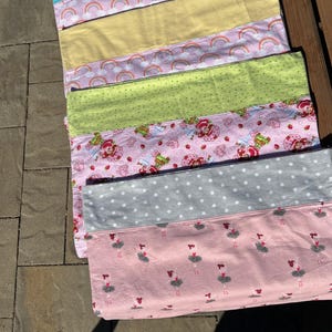 May include: A patchwork quilt with various fabric patterns. The quilt features sections of light blue, yellow, pink with rainbows, green with white dots, pink with strawberries, grey with white dots, and pink with ballerinas.