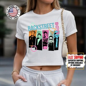 May include: White t-shirt featuring the text "BACKSTREET BOYS" in teal and pink, with a graphic of the band members. The shirt also has a "MADE IN THE USA" logo.