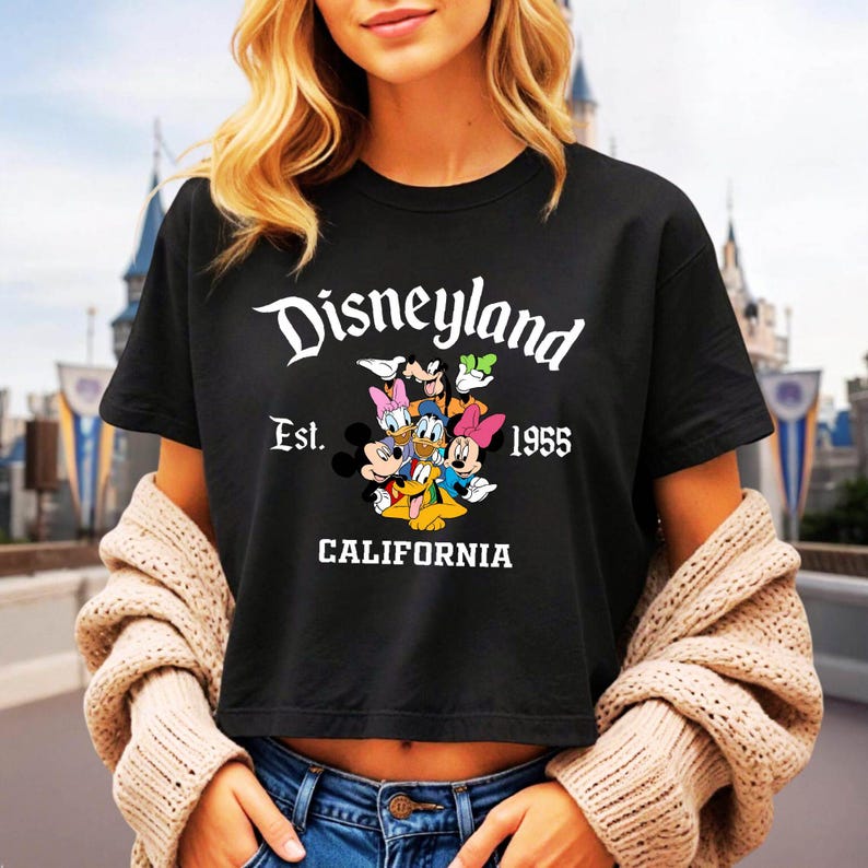 May include: Black t-shirt featuring the Disneyland logo with Mickey Mouse and friends. The shirt includes the text "Est. 1955 CALIFORNIA" in white. The design showcases classic Disney characters in a colorful graphic.