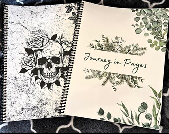 May include: Open spiral-bound journal with a black and white skull and rose design on the left page. The right page features the text "Journey in Pages" surrounded by green botanical illustrations. The journal is open on a patterned surface.