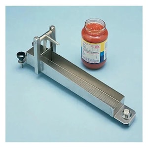 May include: A stainless steel food portioning tool with a graduated trough and a sliding blade. A jar of red sauce sits beside the tool. The tool is designed for precise food measurement and portioning.
