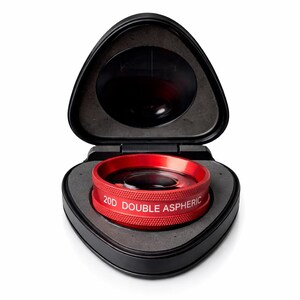 May include: A red 20D Double Aspheric lens sits in an open black triangular case. The lens has the text "20D DOUBLE ASPHERIC" in white. The case's interior is gray, and the lens is circular.