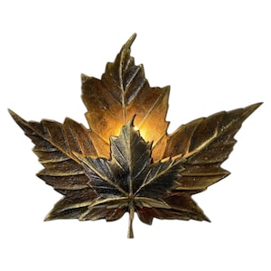 May include: A wall light shaped like a layered maple leaf with a metallic bronze and gold finish. The design features a larger leaf base with a smaller, darker leaf centred on top, creating a dimensional effect with a warm light glow.