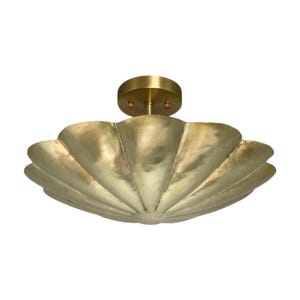 May include: A flush mount ceiling light fixture featuring a wide, scalloped, bowl-shaped shade with a brushed brass finish. The fixture includes a circular canopy at the top, connecting to the center of the metallic, petal-like structure.